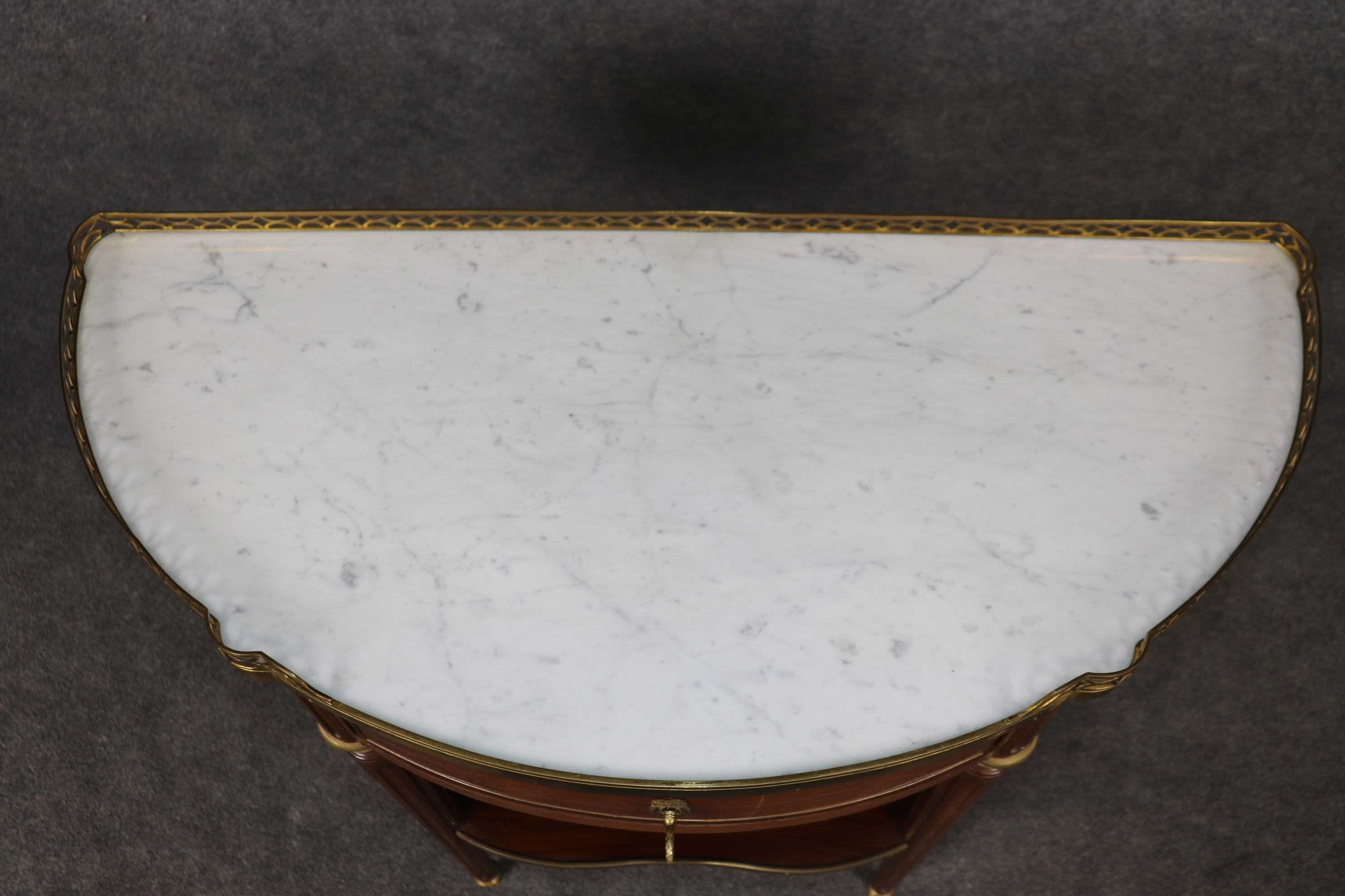 This is a superb ribbon mahogany and Carrara marble top demilune console table with a fantastic bright brass pierced gallery. The table is in good vintage condition and features gorgeous wood quality and tight dove-tailed construction. The table is