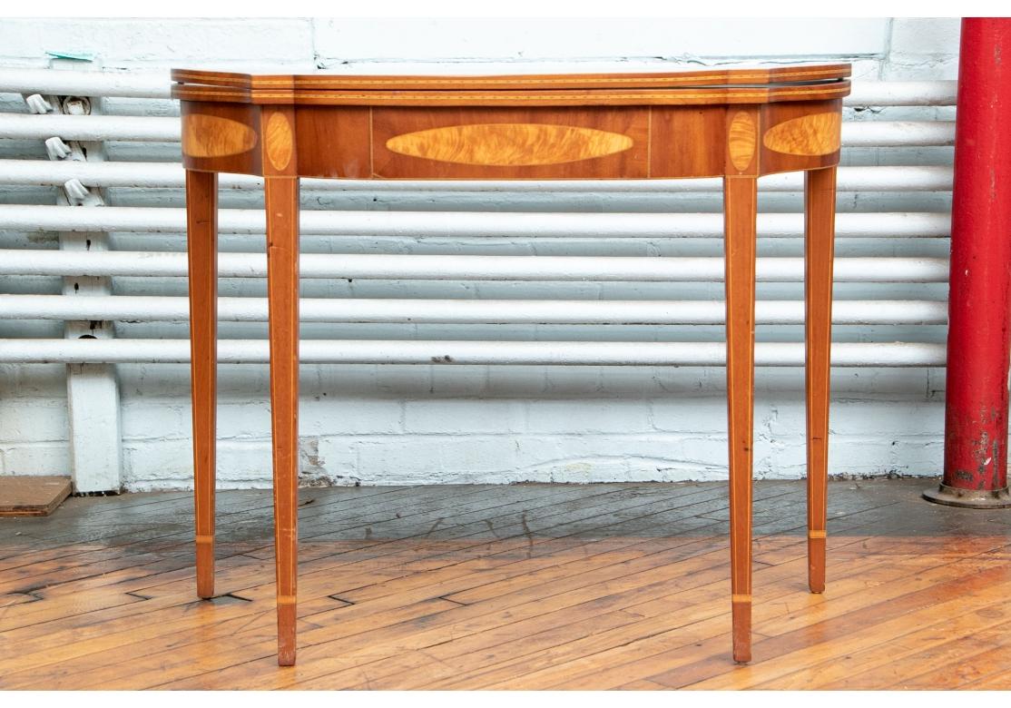 A beautifully crafted and handsome Hepplewhite style flip-games table. A serpentine from mahogany games table with checked sting inlaid top edges. The apron with large oval burled inlays on the front and sides and fine checked string inlays on the