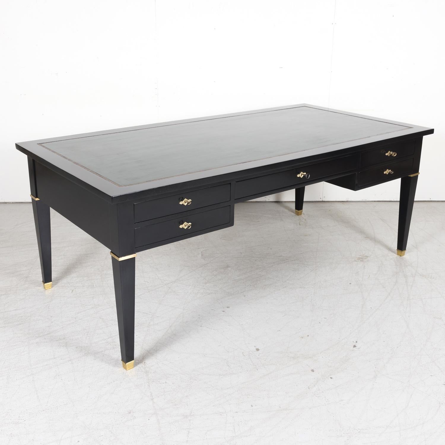 An exceptional mid-20th century Maison Jansen attributed French Louis XVI style bureau plat or desk, circa 1930s. Having an ebonized semi-gloss lacquered finish with the original inset dark forest green leather writing surface with embossed gilding