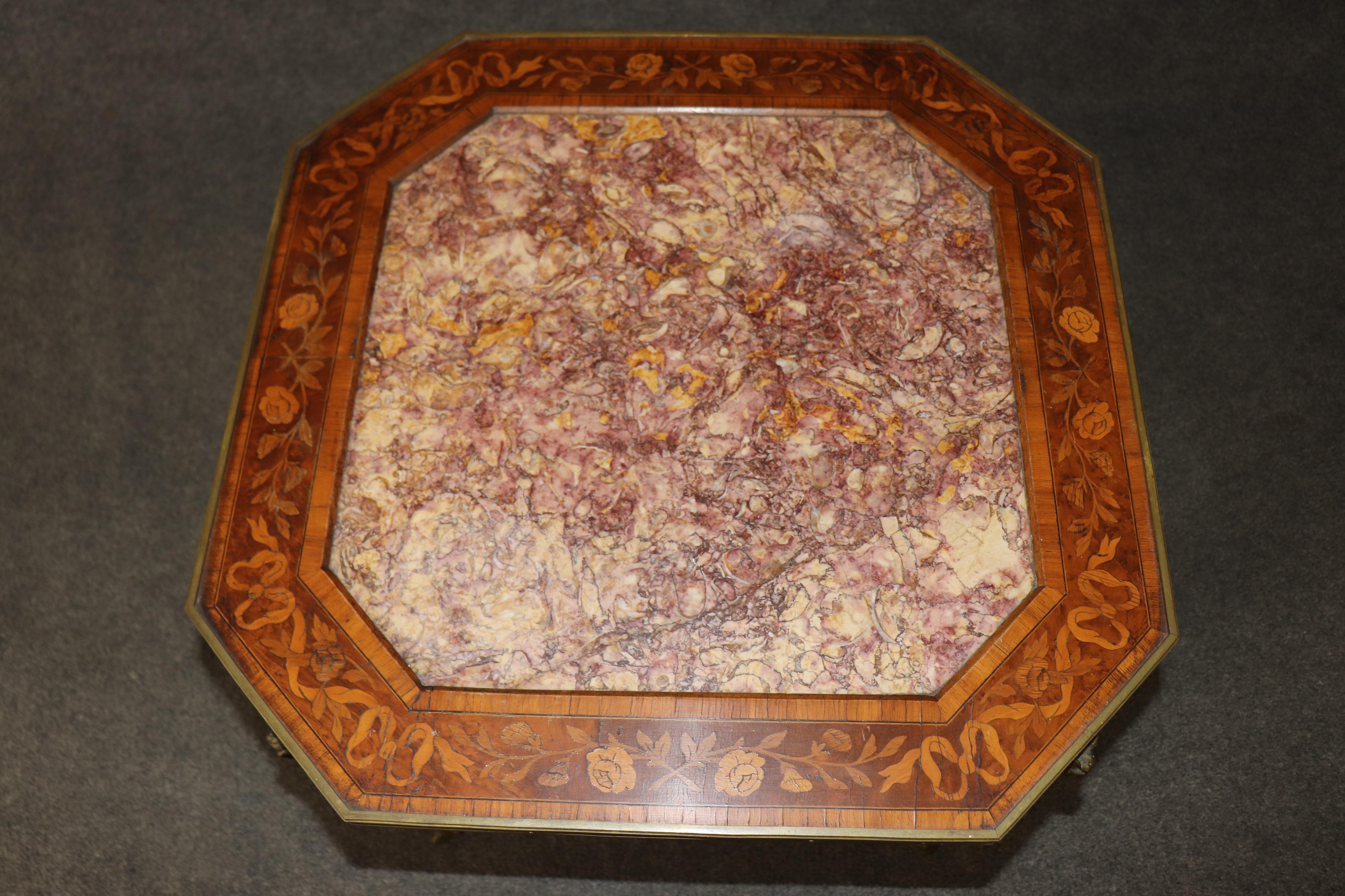 Cette exquise table d'appoint française ancienne témoigne de l'élégance intemporelle de l'artisanat du début du XXe siècle. Elle est ornée d'une marqueterie richement détaillée et d'un superbe plateau octogonal en marbre rose. Les incrustations