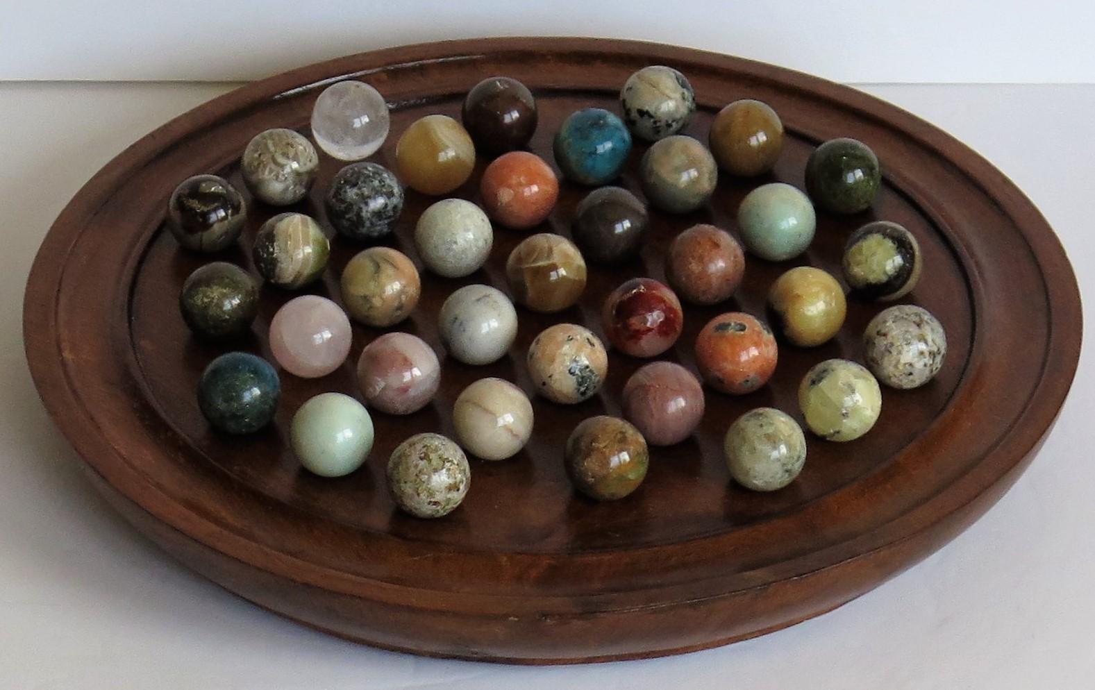 This is a complete board game of 37 hole marble solitaire with a very good 10.38 inch diameter hardwood board and 37 beautiful individual agate mineral stone marbles, which we date to the early 20th century, circa 1920 and probably of French