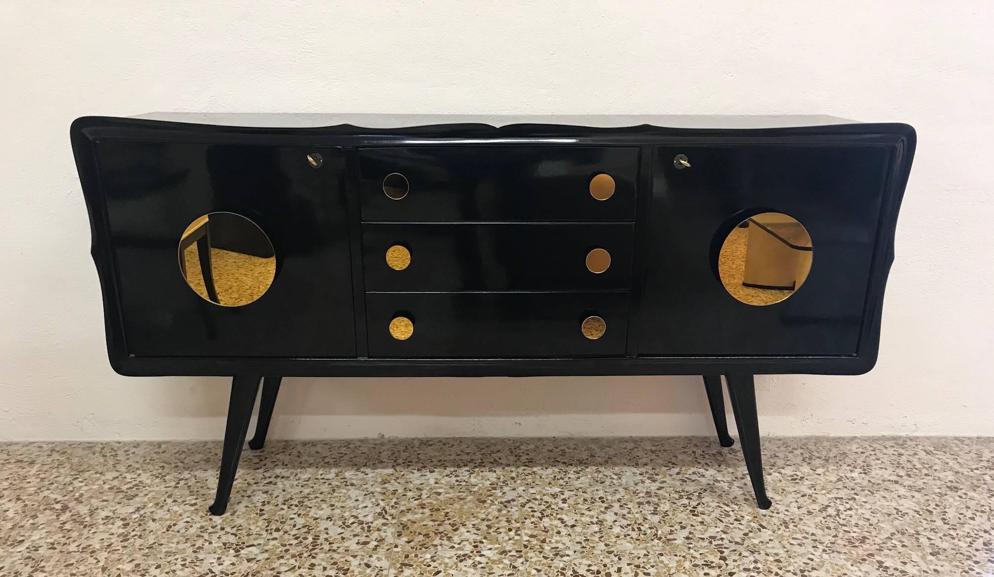 This sideboard was produced in Italy in the 1950s.
The structure is black lacquered and brass keys.
The front is embellished with unique round gold-colored mirrors.