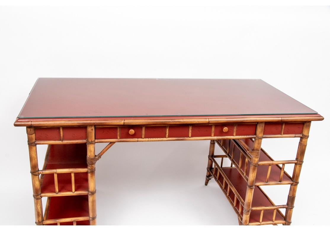Campaign style desk finely crafted in rattan with oxblood red painted surfaces. With a long frieze drop-front drawer and two open shelves with slatted construction on each side and the back. With glass protecting the top.
Measures: Length 70