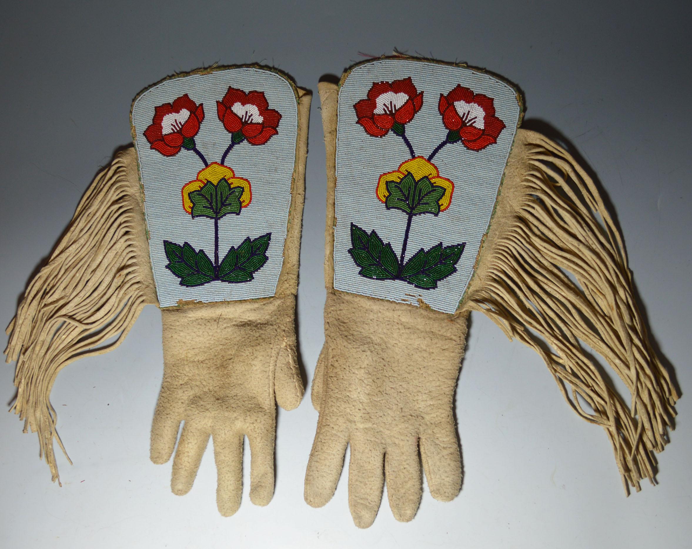 A pair of Native American Crow beaded gauntlets,
buckskin with colored glass beads and cloth interior, 
the cuffs with a floral design in light and dark blue, green, yellow, red and white, 
with a fringe and part cloth lined with printed material
40