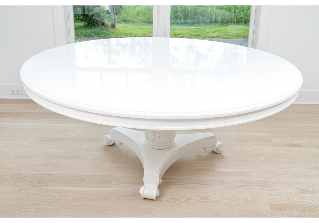A very large and dramatic Neoclassical Style dining table in Snow White color. A professionally finished white lacquered round dining table with prominent carved beaded edge. The table with a bold carved pedestal, tripod legs with conforming beaded