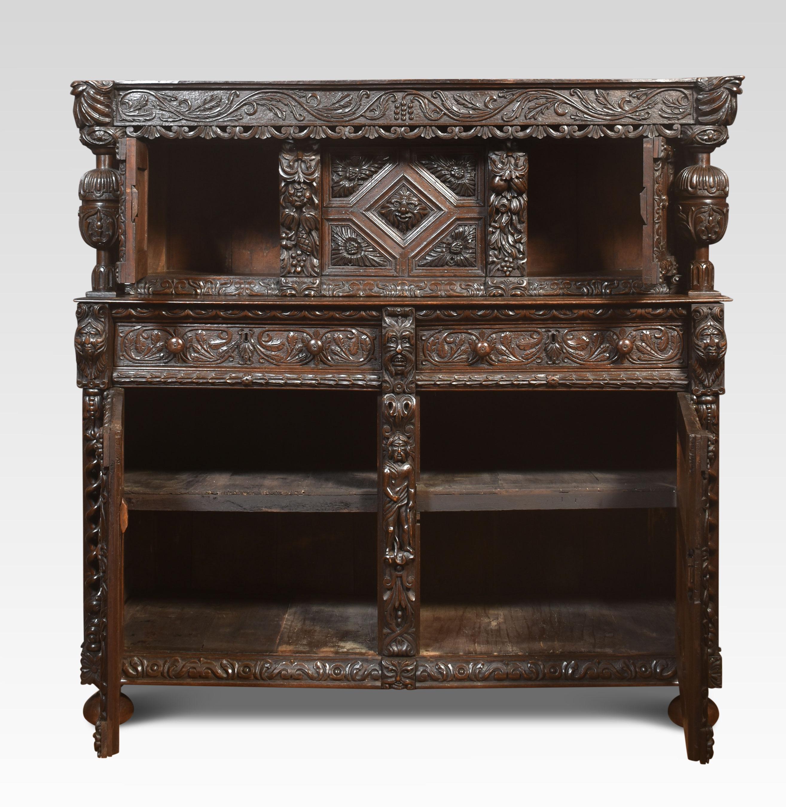 Fine old oak Profusely Carved court cupboard in Elizabethan manor, the frieze with scrolling decoration, with leaf motifs above two panelled doors with decorated panels. Flanked by a pair of cup and cover supports. To the base section with three