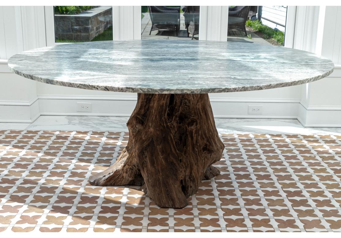 An organic dining table comprised of a variegated grey and white round marble top surmounted on a natural tree root pedestal base. The stone patterning with an Ocean Water type presentation with great movement and appeal. 

Dimensions: 65 1/2
