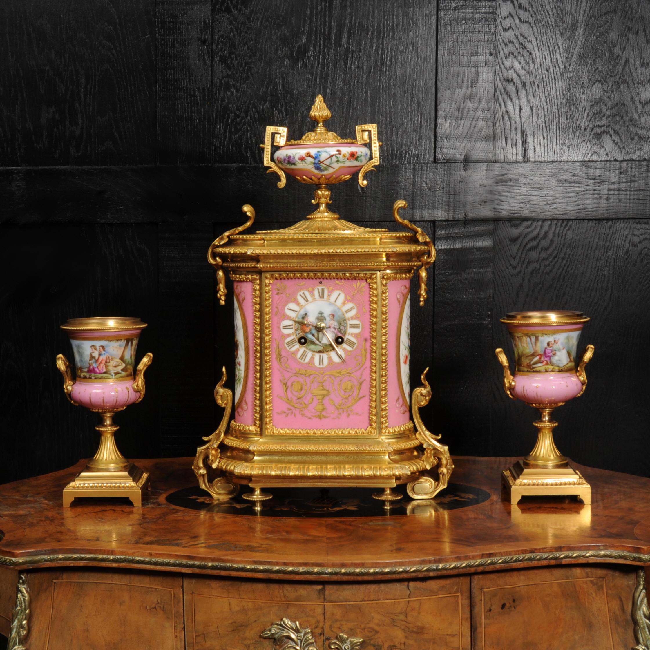 A stunning antique French ormolu clock set, circa 1870, mounted with exquisite Sèvres style porcelain with Rose Pompadour pink ground. Panels to the centre of the dial and the urns feature finely painted scenes of a young couple in a tranquil