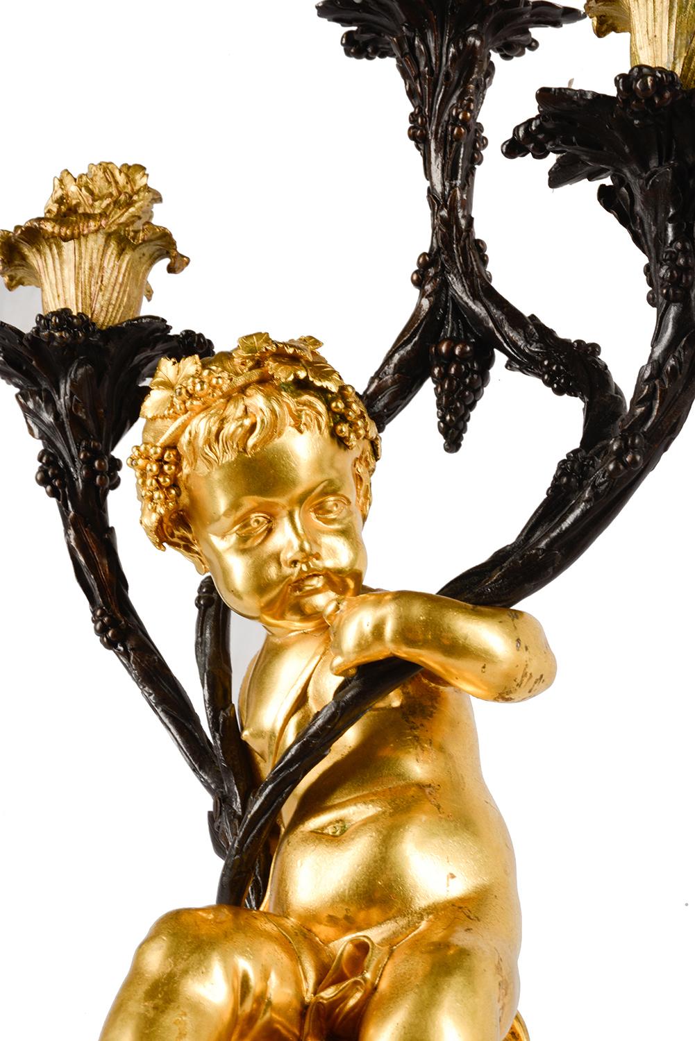 A very good quality pair of 19th century bronze and gilded ormolu three branch candelabra, one modeled as a bacchanalian satyr, the other a putto, out stretched arms holding three branch like candle sconces, mounted on Porphyry plinths with gilded