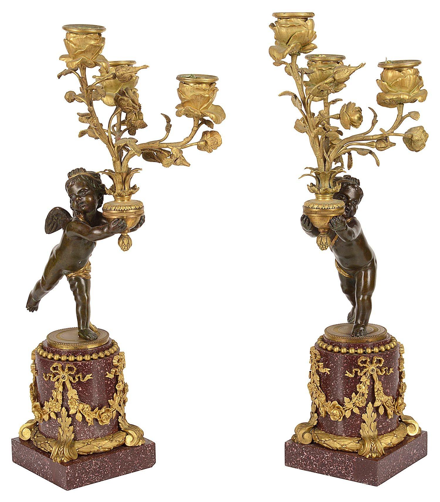 A rare and fine quality pair of 19th Century gilded ormolu, patinated bronze   cherubs, each holding a three branch scrolling foliate candelabra with floral sconces, raised on these wondereful Porphyry pedestal bases with ormolu swag mounts.