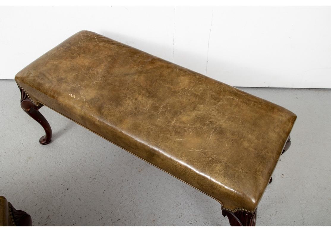 A fine pair of timeworn and very solid feeling Leather Benches. Raised on Chippendale style carved cabriole legs in a dark stain with carved ribbed and scrolled knees and pad feet. Upholstered in a mottled olive-brown leather with nail-head trim on