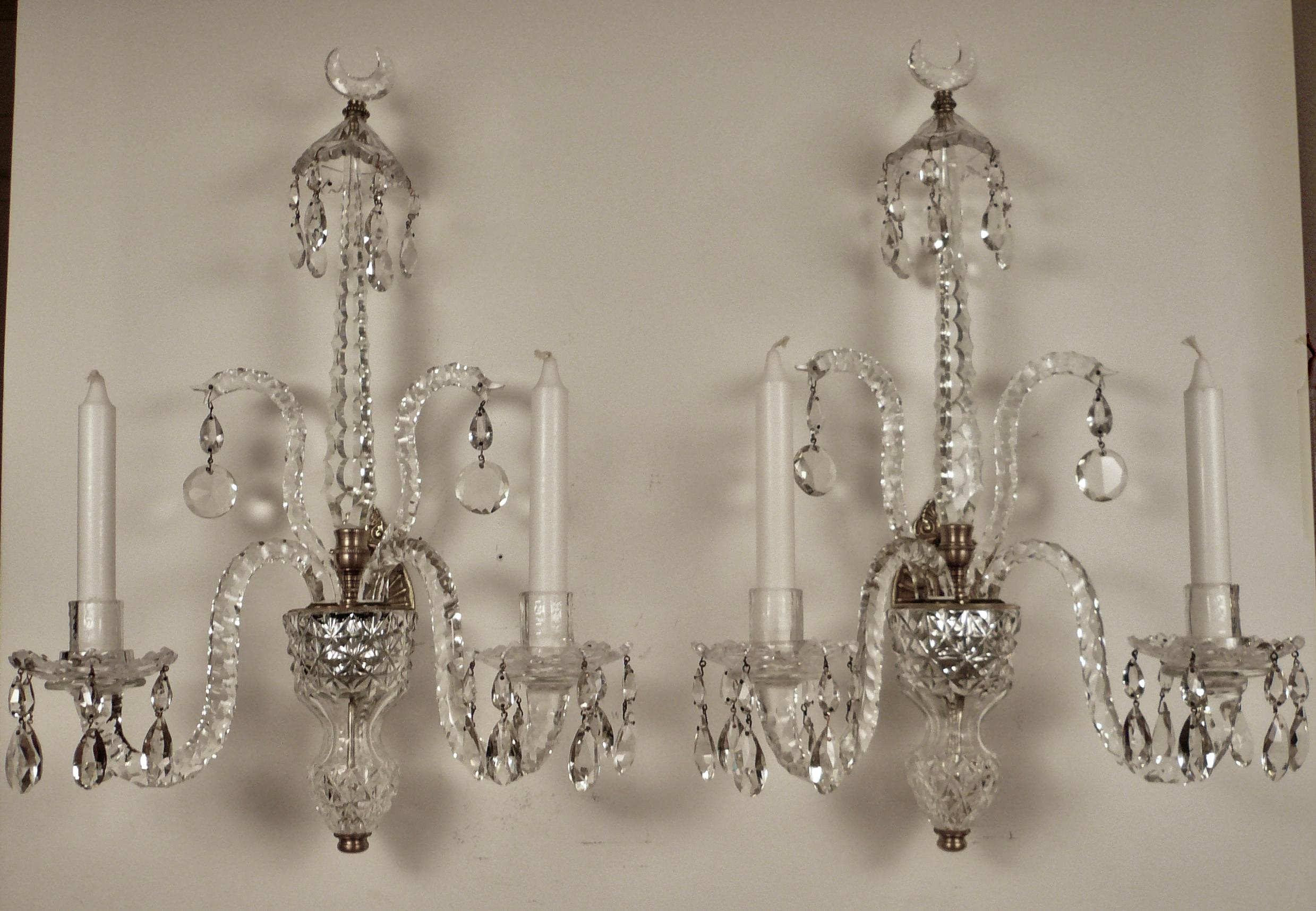 This fine pair of two light cut crystal sconces are beautifully proportioned and of the finest quality. They feature pear shaped prisms, snake scrolls, faceted spires, and crescent form finials.