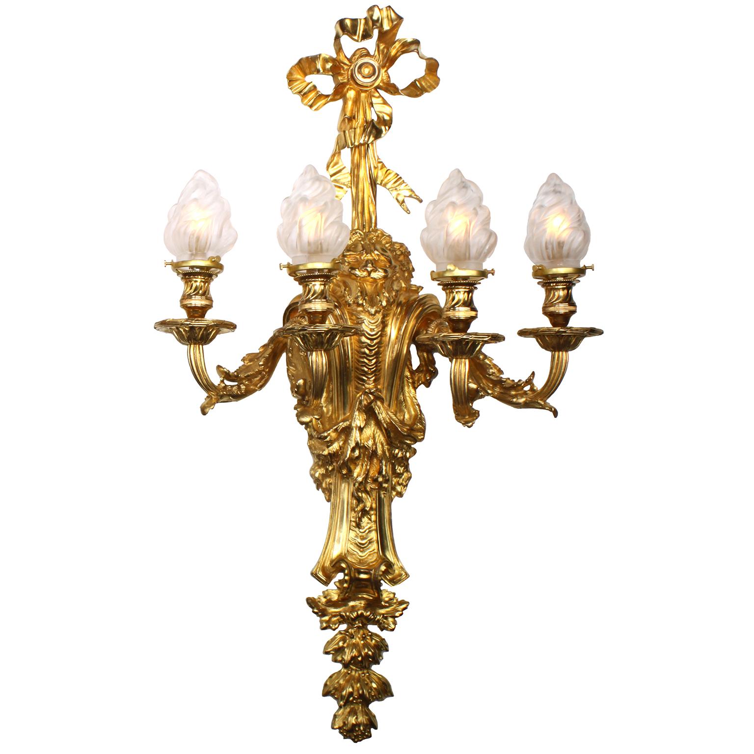 Ein sehr feines und beeindruckendes Paar französischer vierflammiger Wandleuchter aus vergoldeter Bronze im Regénce-Stil (19./20. Jh.). Jede Ormolu-Lumière trägt in der Mitte eine Maske mit Löwenfell, darüber vier ausgestellte, verschnörkelte