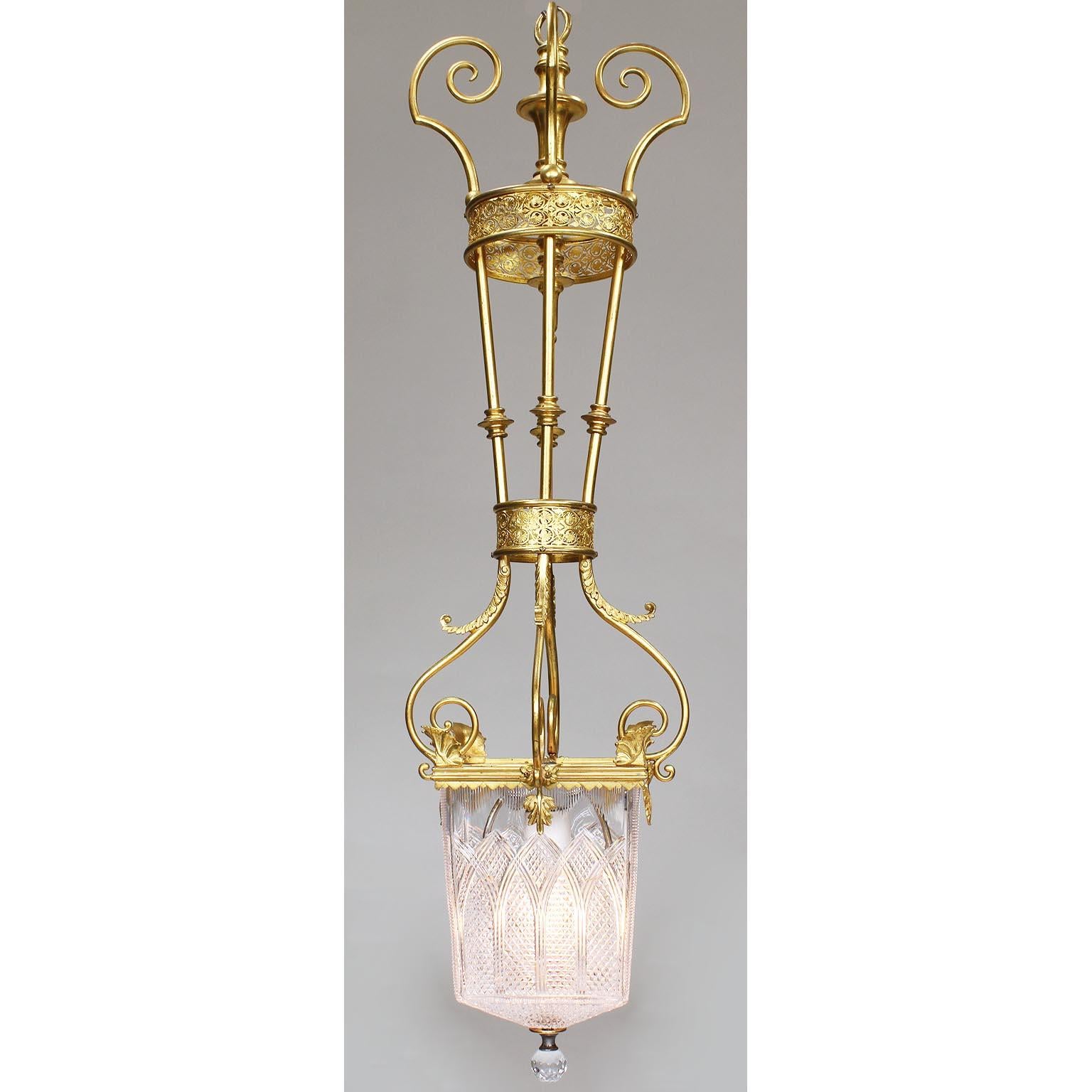 A fine pair of French 19th-20th century Belle Époque neoclassical style gilt-metal and cut-molded-glass hanging lanterns. The single-light scrolled finely chased gilt-metal body with scrolls, leaves and acanthus supporting cut-glass shade ending