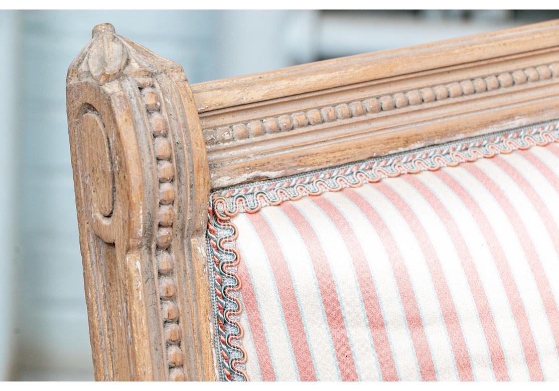 Very well constructed settees with carved frames in pale gray wash over natural wood, circa 1920s. With beaded crest rails and sloping arms with carved finials. The scrolled arm ends sloping into the fluted legs with carved leaves. With a beaded