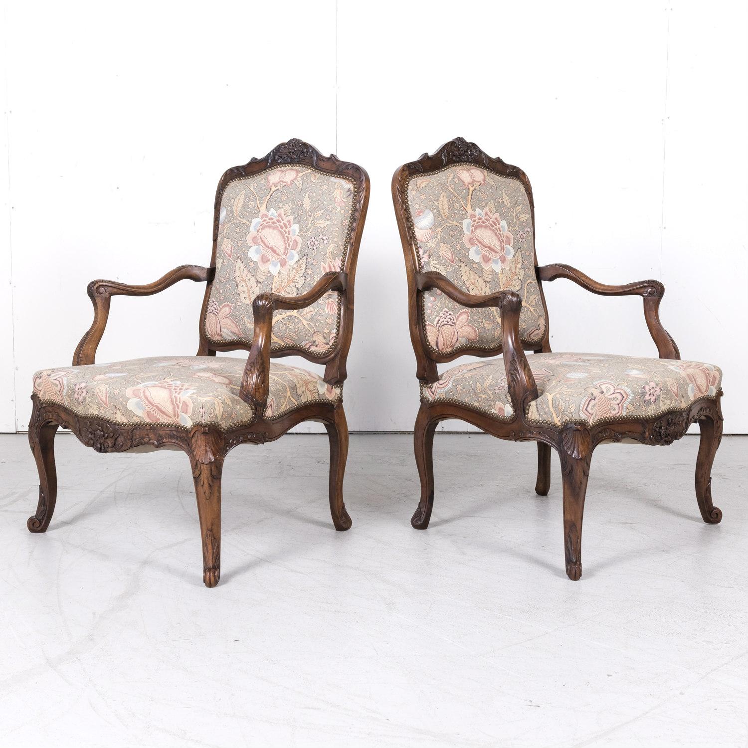 A fine pair of carved 18th century Louis XV period fauteuils handcrafted in Lyon of solid walnut, circa mid-1700s. Featuring a shaped back with a crest of finely carved floral and foliate motifs and elegant scrolling arms with carved acanthus plumes