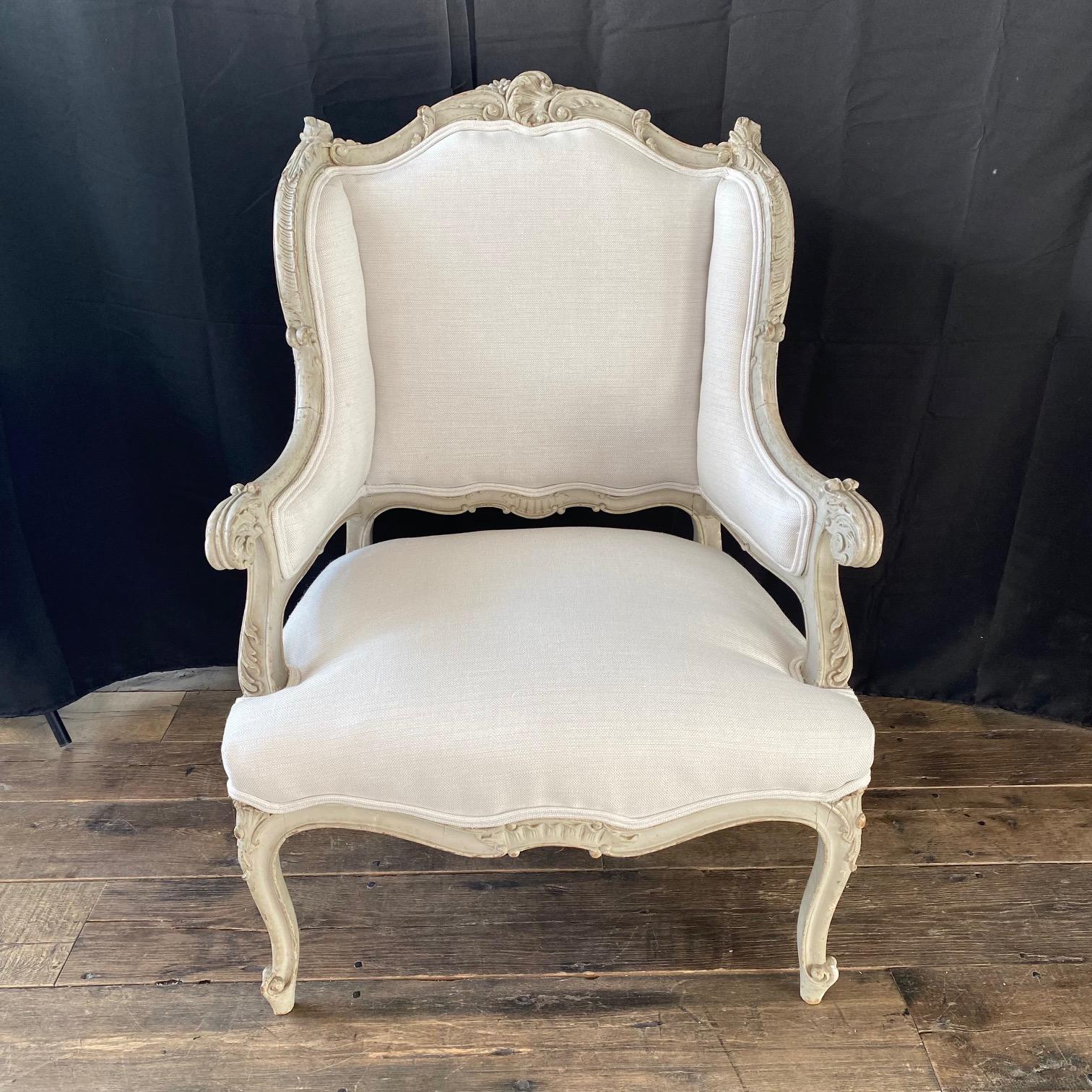 Stunning pair of painted and exquisitely carved French 19th century Louis XV armchairs, wing chairs or bergeres. Beautiful original pale grayish white paint, with new upholstery in high quality complementary neutral white with a touch of the same