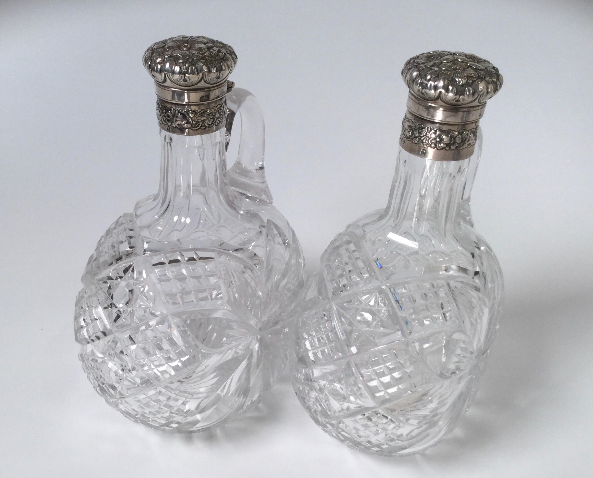A pair of sterling mounted cut glass decanters with handles. The jug form with exceptional cutting in American brilliant glass attributed to Hawkes. The Gorham hallmarked sterling repousse lids which lock and unlock by turning the caps.