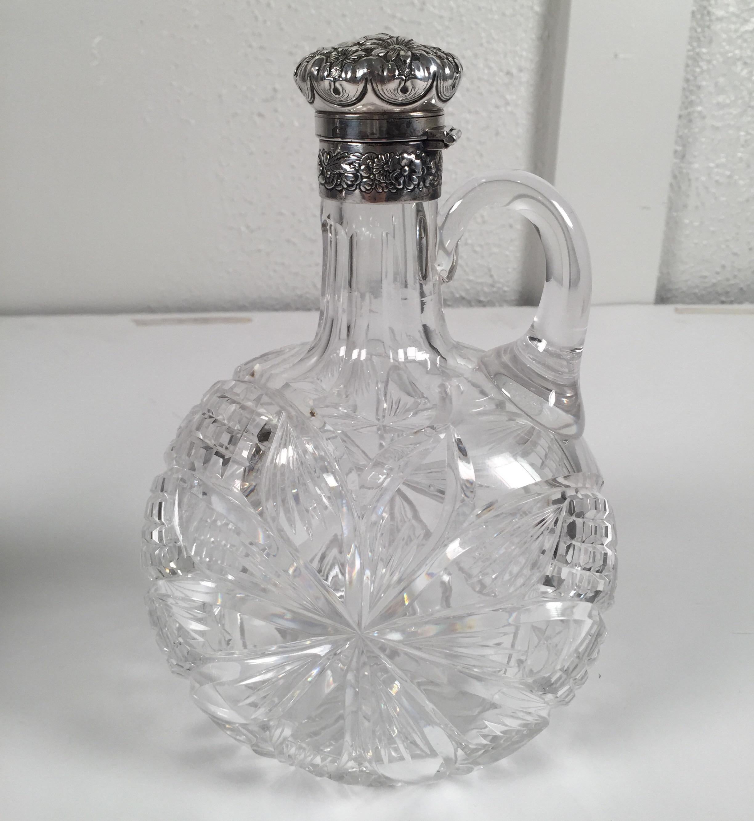 A pair of sterling mounted cut glass decanters with handles. The jug form with exceptional cutting in American brilliant glass attributed to Hawkes. The Gorham hallmarked sterling repousse lids which lock and unlock by turning the caps.