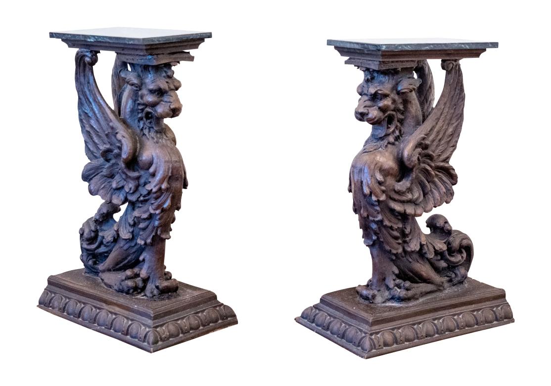 Large finely carved wood seated griffins mounted on bases with a carved egg-and-dart edge on three sides. Each fierce griffin is presented seated with elaborately carved outstretched wings and three-dimensional feathers. With attached marble tops. 