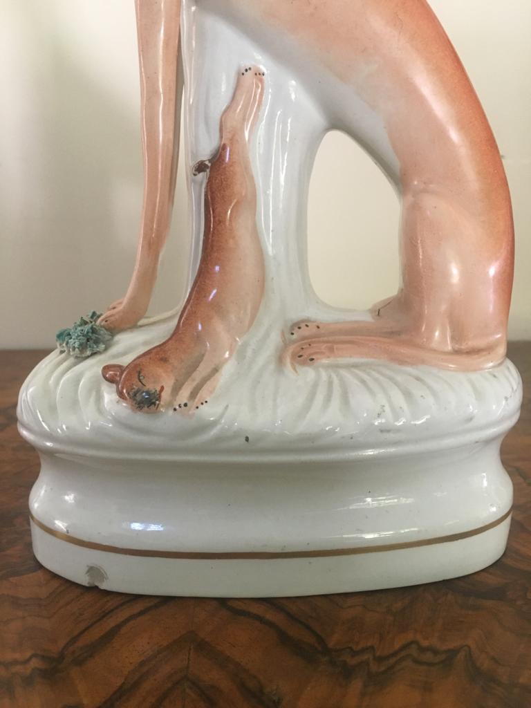 A fine pair of antique Staffordshire greyhounds which are a striking pair, peachy, white and gold in color both having rabbits standing on an oval base.

One greyhound has a small chip to the base which is evident in the pictures, otherwise in