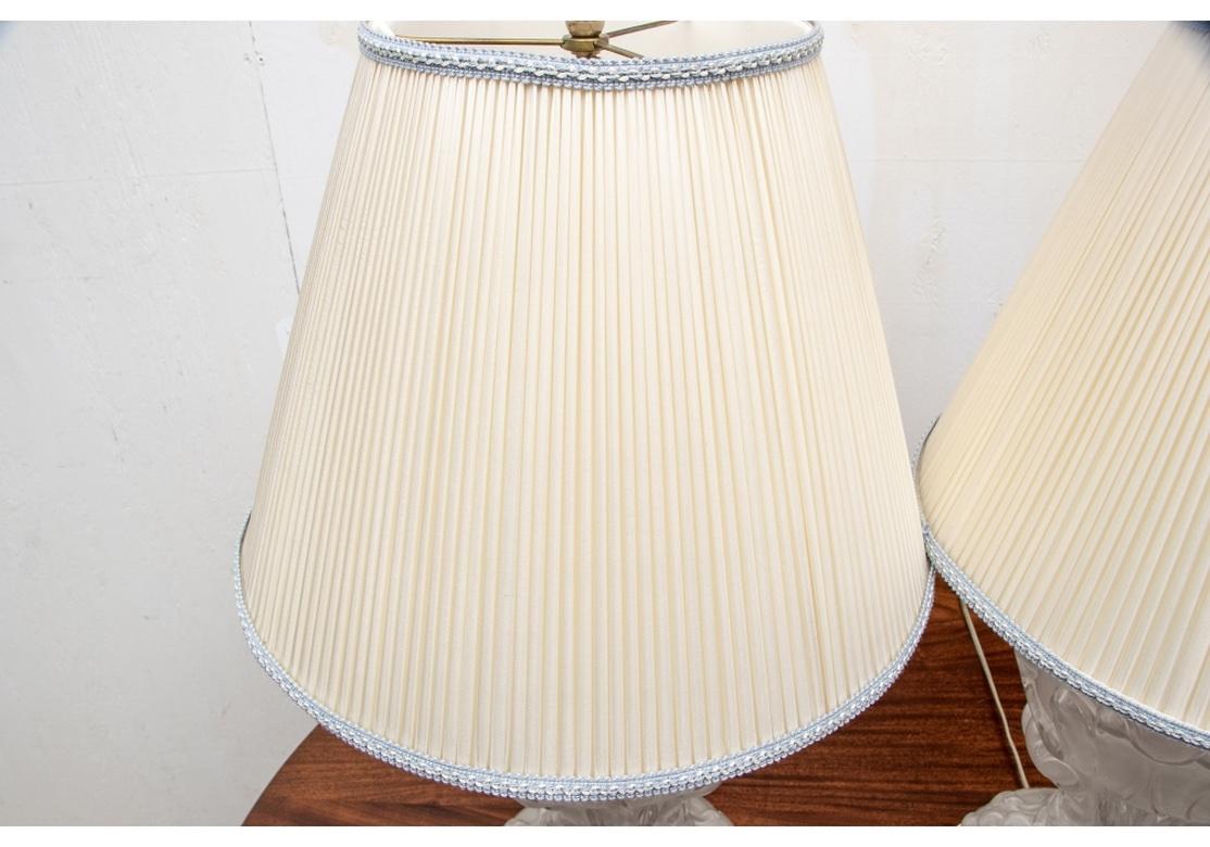 A pair of large and sensational molded and frosted glass lamps. Baluster shapes with high relief acanthus leaves around the top sphere on a scrolled support. On a leafy base mounted on a silver gilt wood base. With white pleated silk shades with