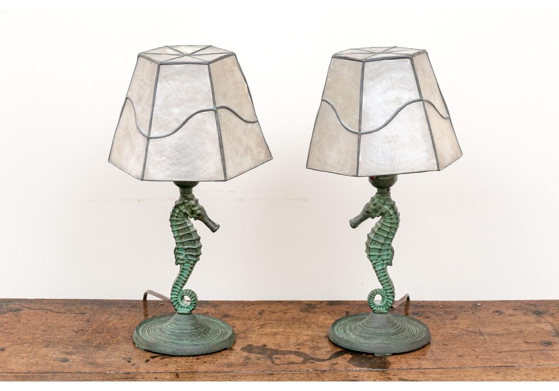 A detailed and well cast pair of Sea Horse Table Lamps with Capiz Shell Octagonal Shades. The bases have an enhancing deep green oxidation to the bronze and the shades have a delicate and decorative tracery frame, likely brass. 

Each Lamp measures