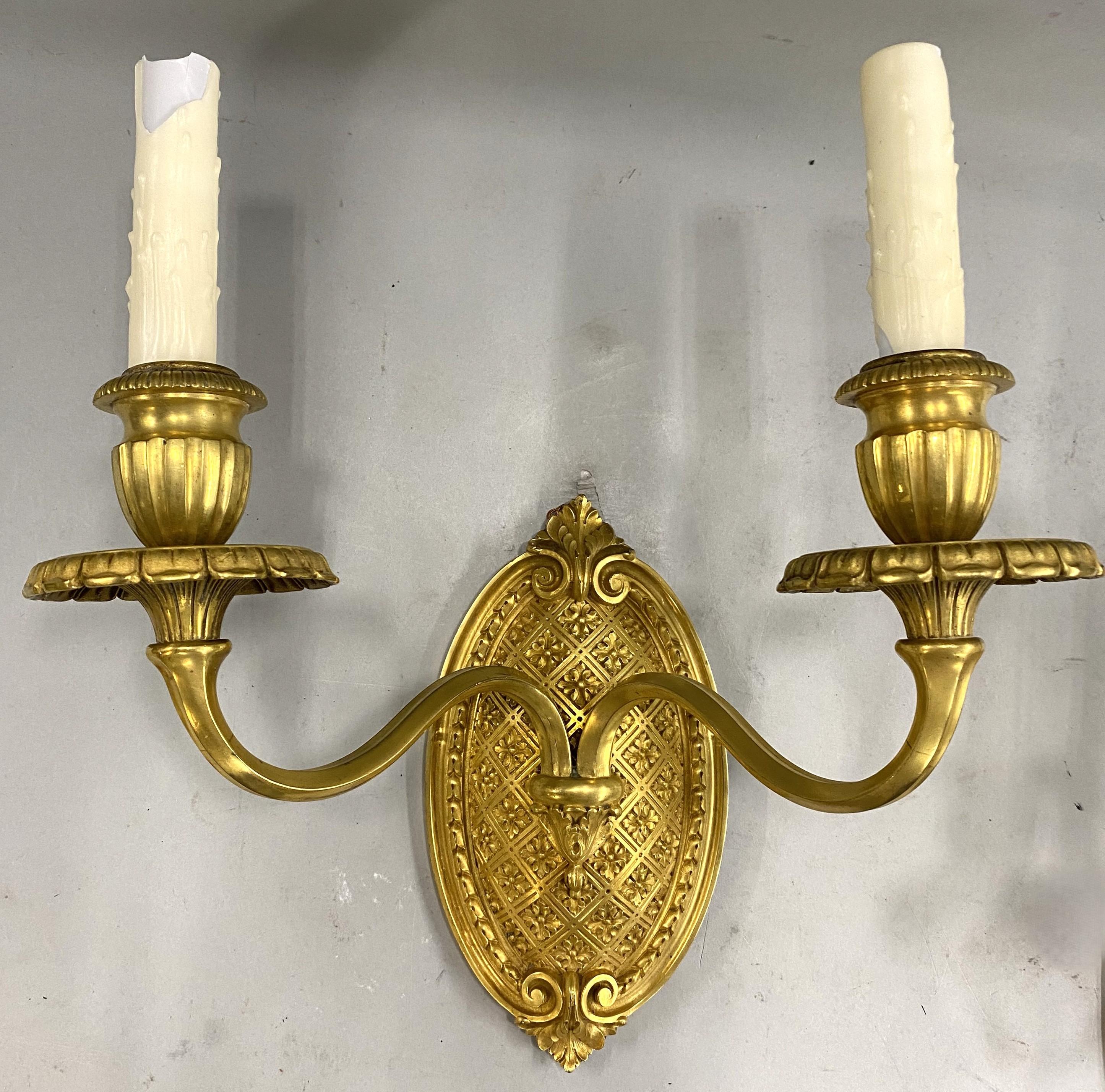 Fino par de apliques de pared de dos luces electrificados de bronce dorado sobre decorativos soportes de pared ovalados, con la marca del fabricante Caldwell & Co en forma de C de diamante estampada en el reverso. Edward F. Caldwell & Co., de Nueva