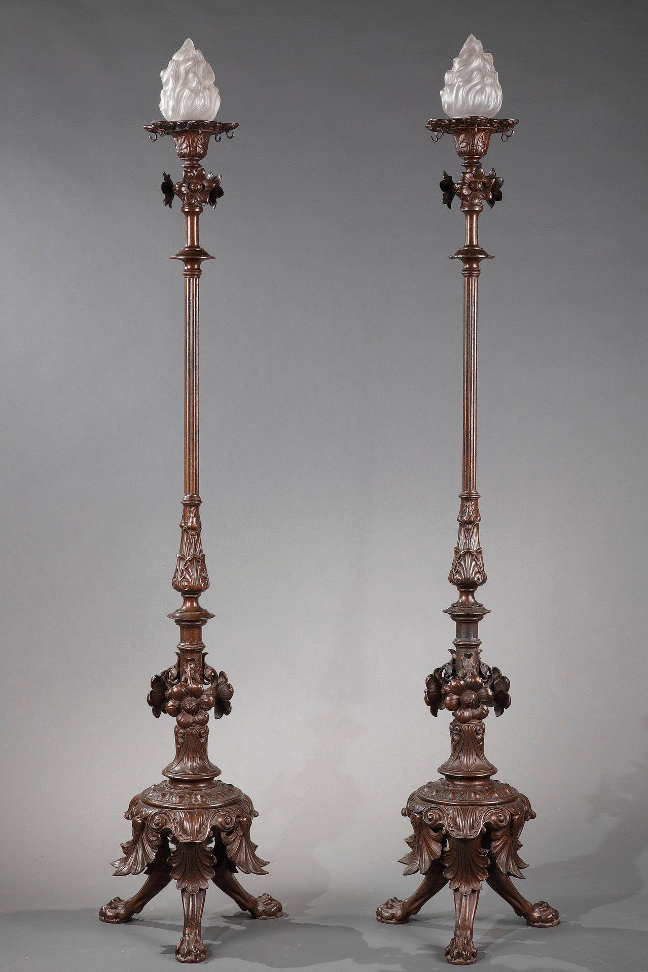 A fin pair of cast iron floor lamps, toped by a flame-shaped light, and adorned with a vegetal decoration made of flowers and leaves, ending with a base composed of three lion paws.