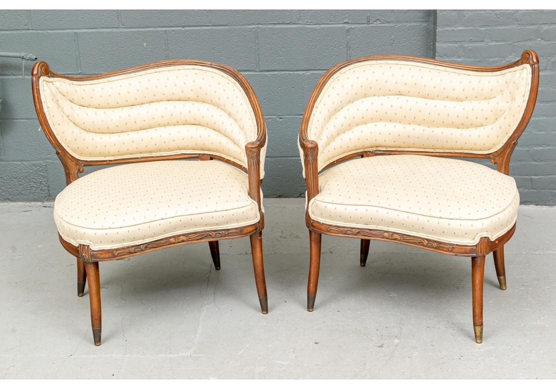 Fine pair of asymmetrical wave back lounge chairs dating from the midcentury era and epitomizing the Hollywood Regency style. Very solid feeling and comfortable the pair have triple tufted wave backs, carved fruitwood finish frames and tapering