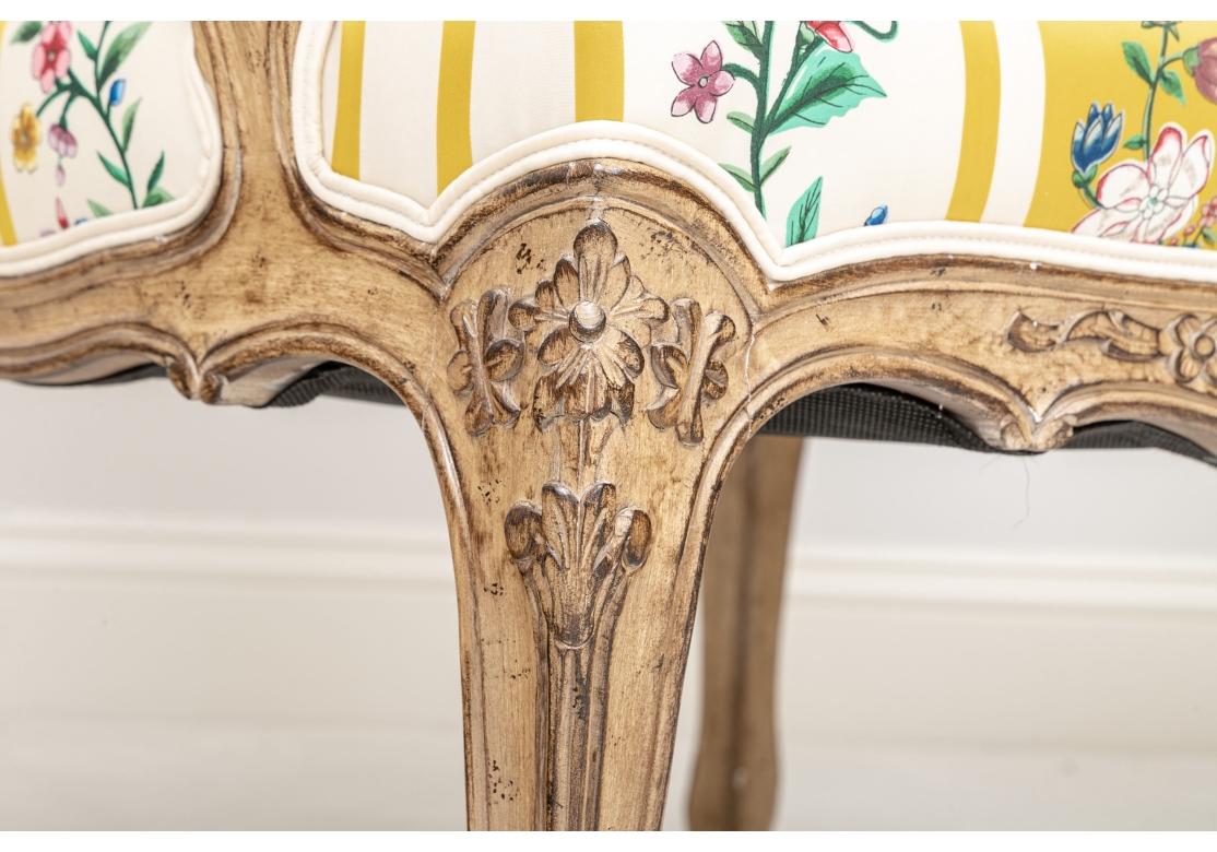 A very fine and colorful pair of Custom Bergeres with good size, handsome frames and exceptional color. The Tan painted frames with intentional distressing and fine floral carved details with arm manchettes, and the bright silk type fabric in a