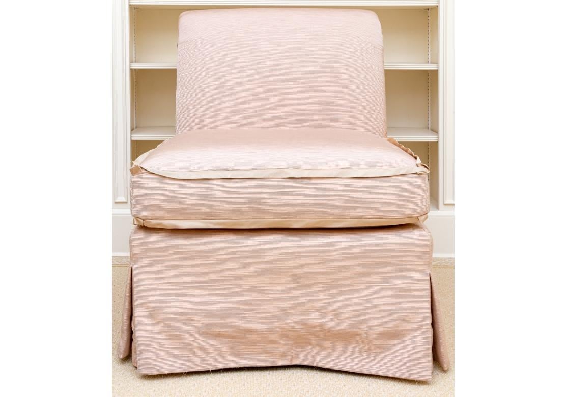 Hollywood Regency style Pair of Slipper chairs in a custom  treatment with Slub  type Pale Pink fabric with a rich textured feel. The backs with buttoned roll tops and the seat cushions with stylish contrasting tan upturned ribbon edging.