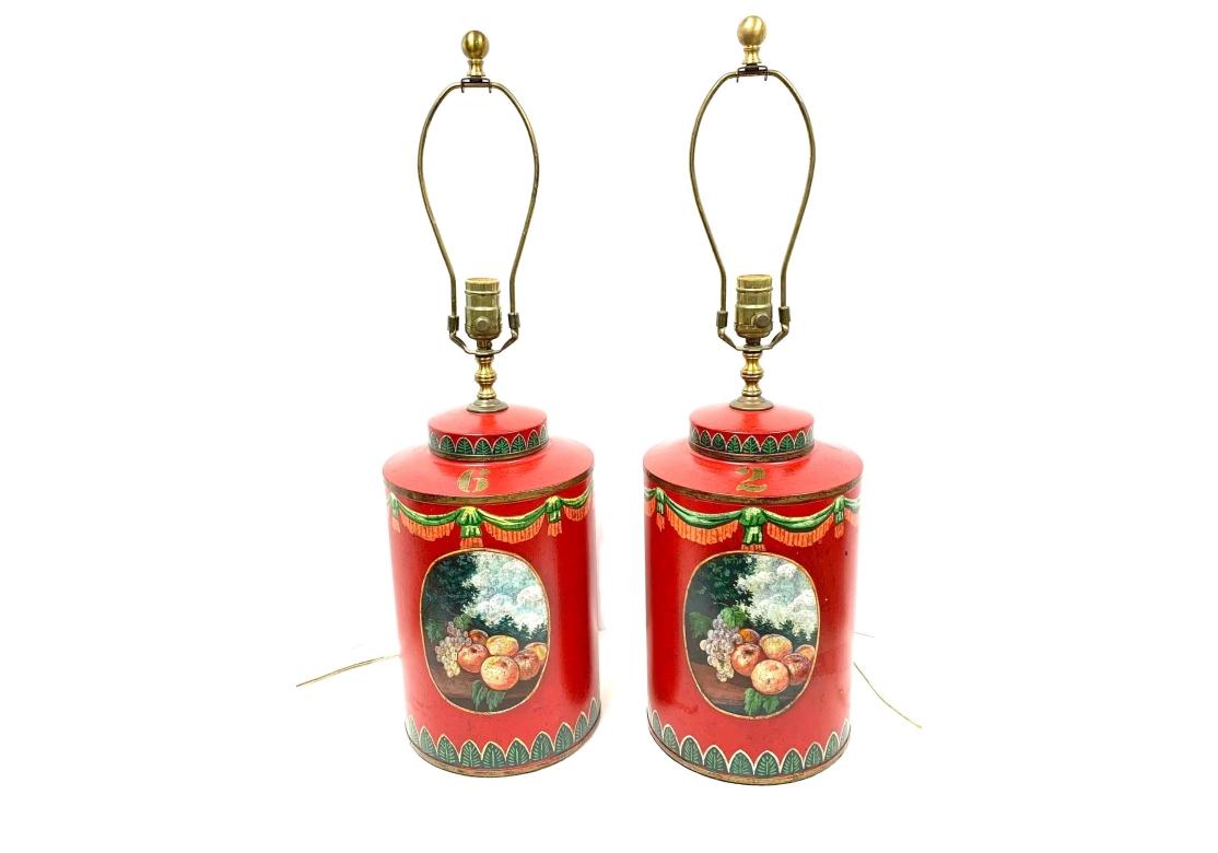 Attractive decorative tea canisters in bright orange red with colorful details. Each has an oval panel with fruits in a landscape setting. Green and peach tone swags frame the tops and bands of green leaves around the bases. The harps have ball