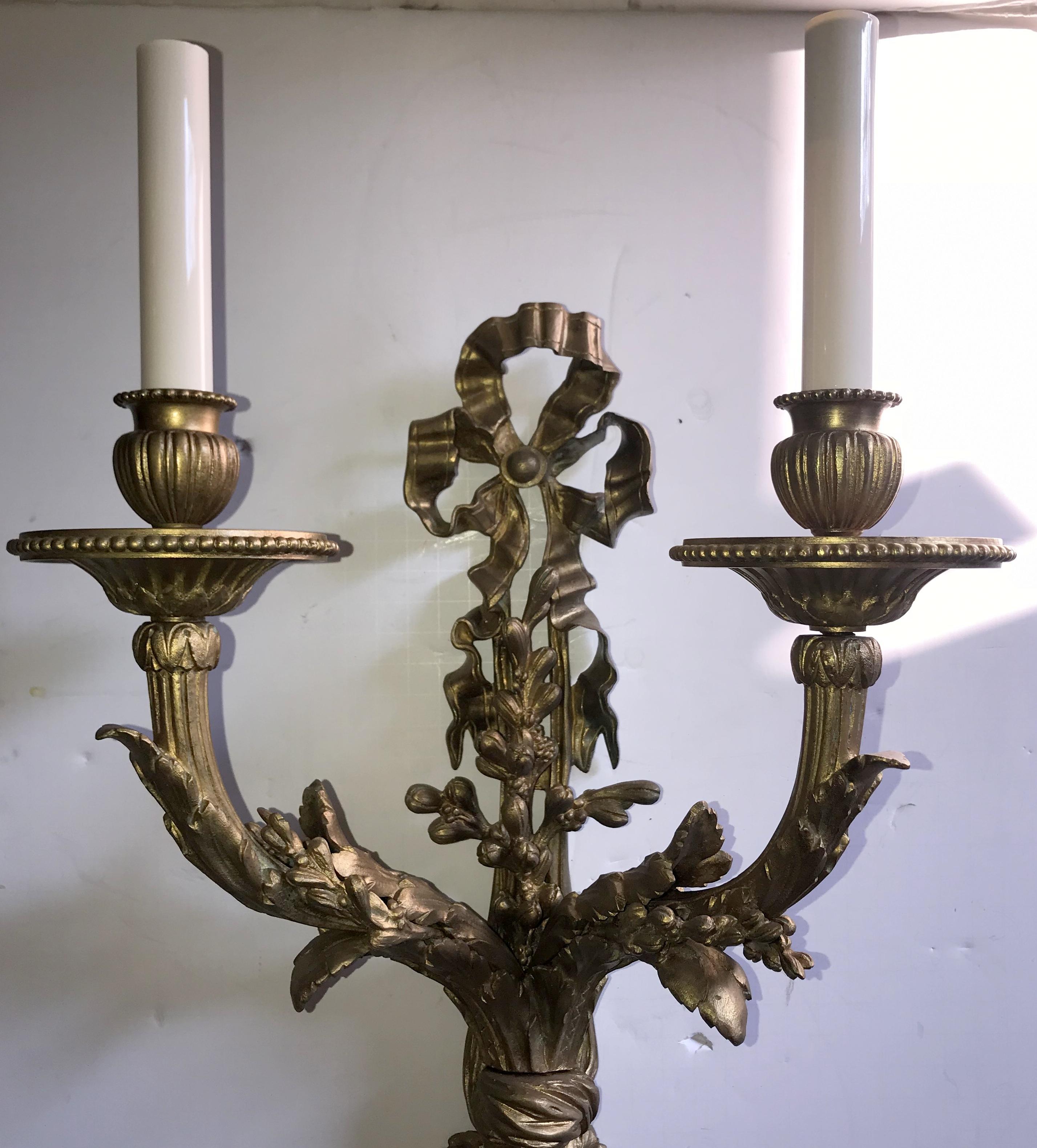 An elegant pair of bow top sconces, circa early 20th century, French bronze with a wonderful aged patina. The bow with the cascading ribbons entwining the beautiful floral filigree and seed detail along both arms and the center finish with the
