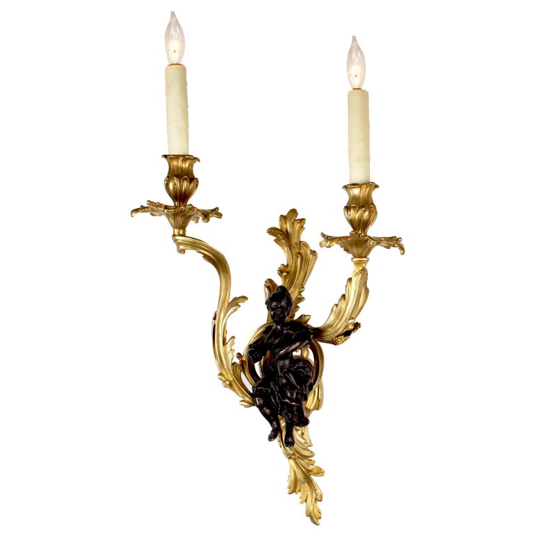 A fine and charming pair of French 19th-20th century Louis XV style gilt and patinated bronze figural two-light wall sconces. The ornate scrolled gilt bronze candle- arms, each centered with a patinated bronze figure of a young boy and a young girl.
