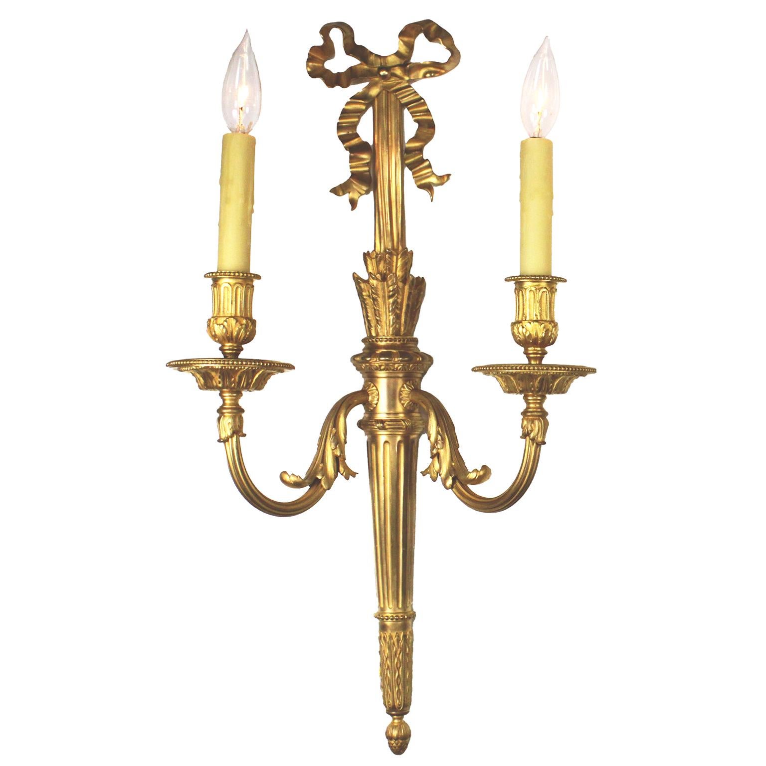 Finos apliques (lámparas) de pared de dos luces de estilo neoclásico Luis XVI francés del siglo XIX-XX. Los apliques, alargados y de ormolina, tienen una placa posterior en forma de antorcha, cada una de las cuales emite dos brazos de vela en forma