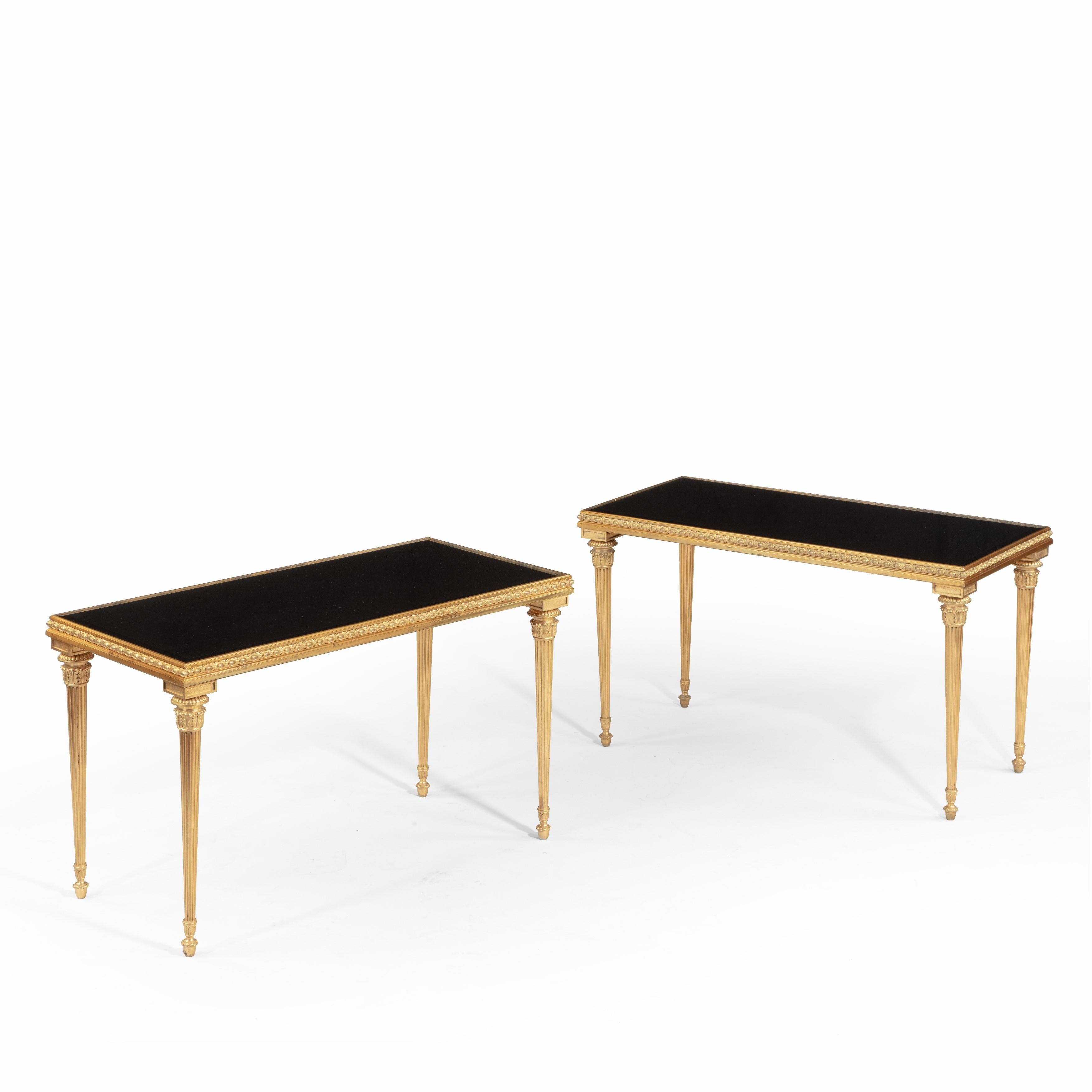 A fine pair of French ormolu low side tables, of rectangular form with bead and ribbon borders above tapering legs in the form of classical flambeaux, with later black glass tops, circa 1920.
 
