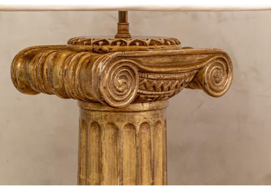 Large and fine pair of gilt wood column lamps in Ionic form in very good condition. The pair have fluted columns, Stylized Ionic capitals with carved design, adjustable height hardware and fine quality Ecru pleated and lined shades. 
Each lamp