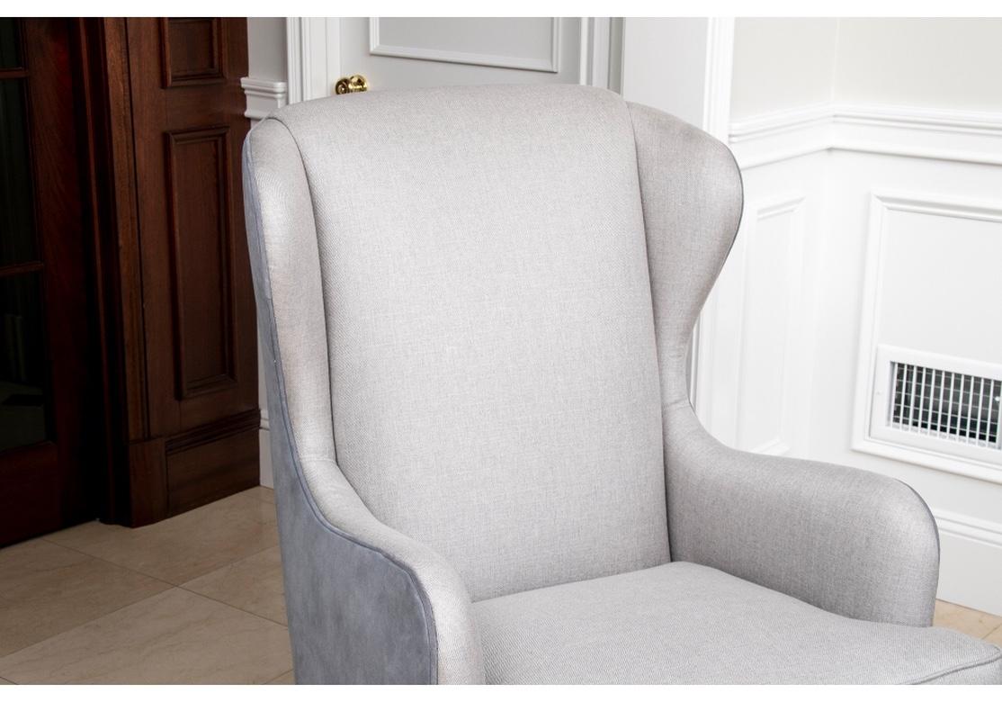 The tall backs with curved sloping arms. The front upholstered in a pale gray tweed fabric, the sides and back in a dusty blue-gray suede. Raised on square tapering blond wood legs, the back ones splayed. 
Measures: H. 43