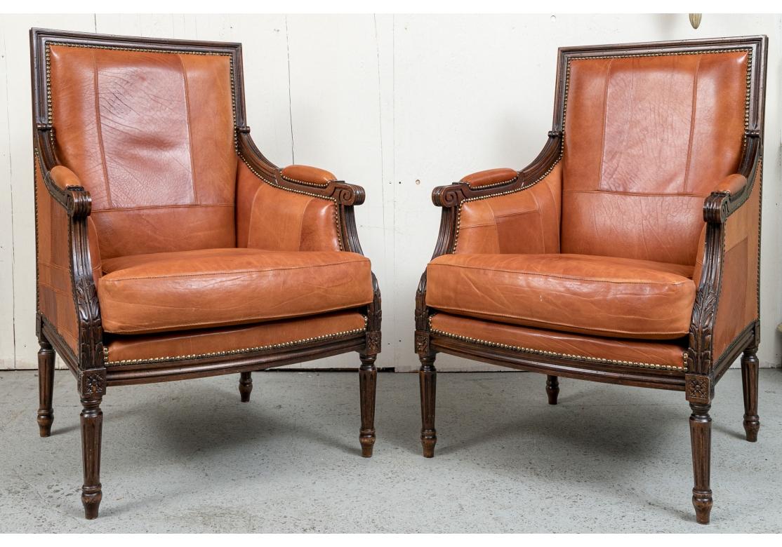Fine pair of Italian Club Chairs upholstered in Caramel top-stitched paneled leather with loose seat, arm manchettes, straight back, carved and fluted arms, loose seat cushion, brass tack decorated and resting on fluted legs. Made by Buying &