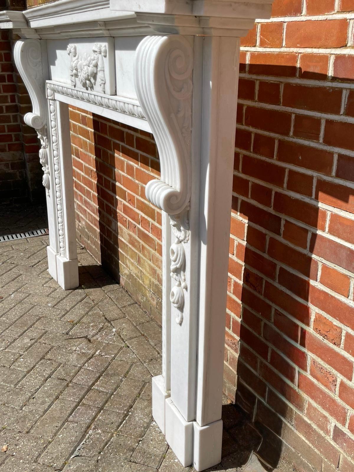 Fine pair of large antique Edwardian quality carved white marble fireplaces having an inverted breakfront top with a double moulded edge supported by large carved marble scrolls, carved bows & fruit.

Exemplary first class examples in fabulous