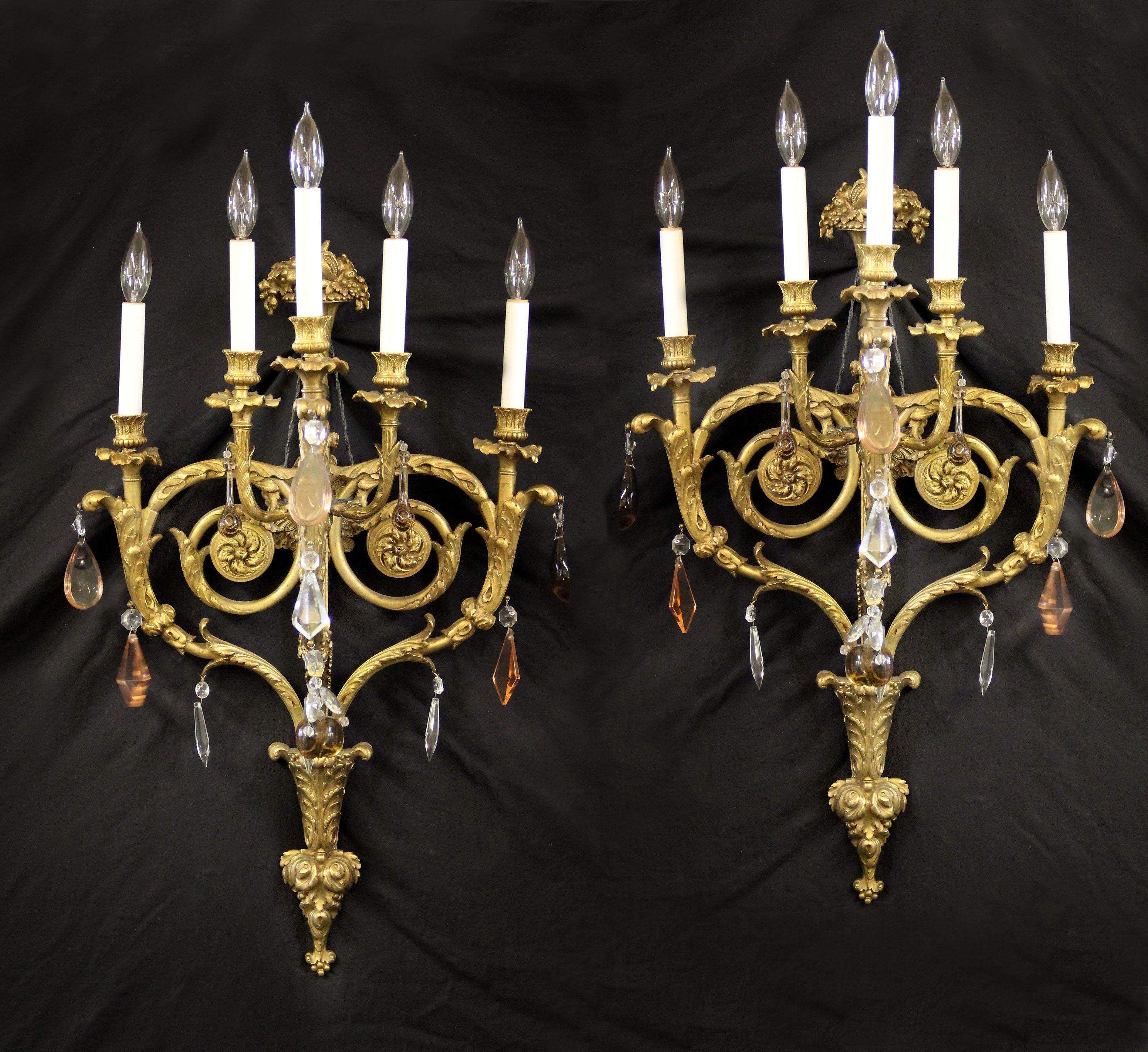 A fine quality pair of late 19th century gilt bronze and French crystal five-light sconces.

Multifaceted and shaped crystal, foliate-scrolled arms and backplate, cantered by a cornucopia with produce and flowers, five-tiered lights.