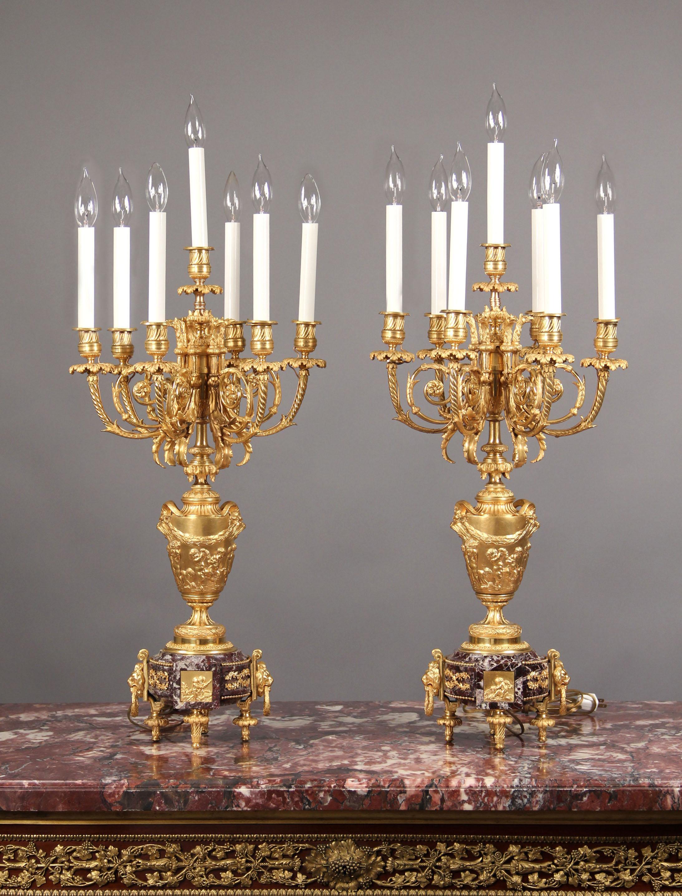 A fine pair of late 19th century gilt bronze seven light candelabra,

after Claude-Michel Clodion.

Each as a vase cast in high relief with a procession of putti, with a pair of grotesque mask handles supporting laurel festoons,with six scrolled