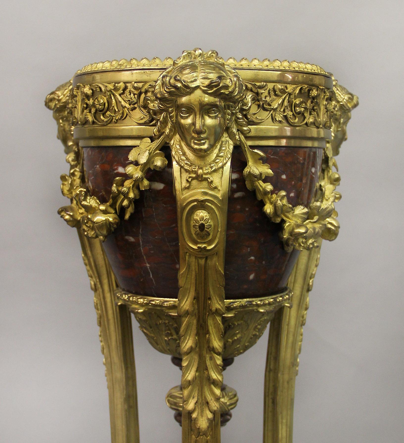 An excellent quality pair of late 19th century Regence Style Napoleon III gilt bronze and rouge griotte marble Jardinieres-on-stands

Possibly cast by Henri Picard

Each tin lined tapering jardinière supported by triple Apollo mask suspending