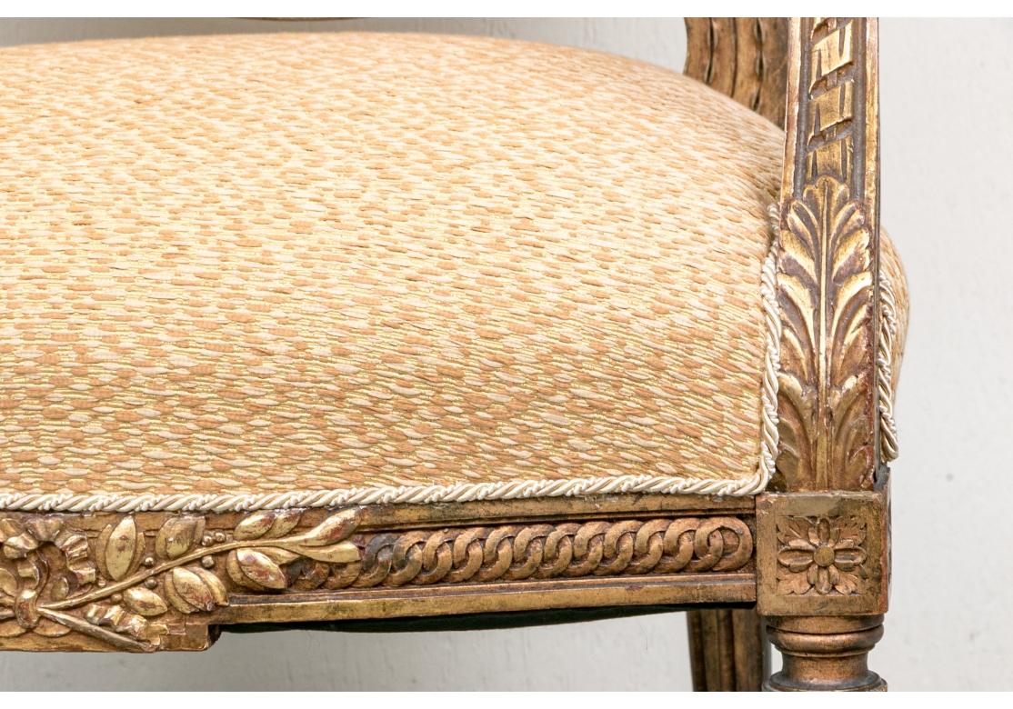 Fine Pair of custom upholstered Antique French Armchairs with gilt and intricately carved frames, frame with overall Laurel Leaf, Scroll and Foliate carving,  fluted and tapered round legs, arm manchettes and Classic French form. The Pair have been