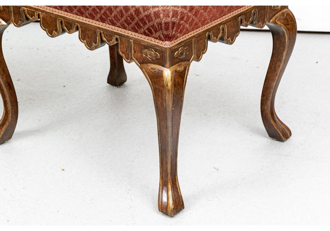 The frames in a striking Burl stain with carved scalloped skirt rails. Raised on angular cabriole legs. The frames and legs with antiqued gilt edges and details for an elegant look. The tops upholstered in a burgundy and tan lattice pattern fabric.