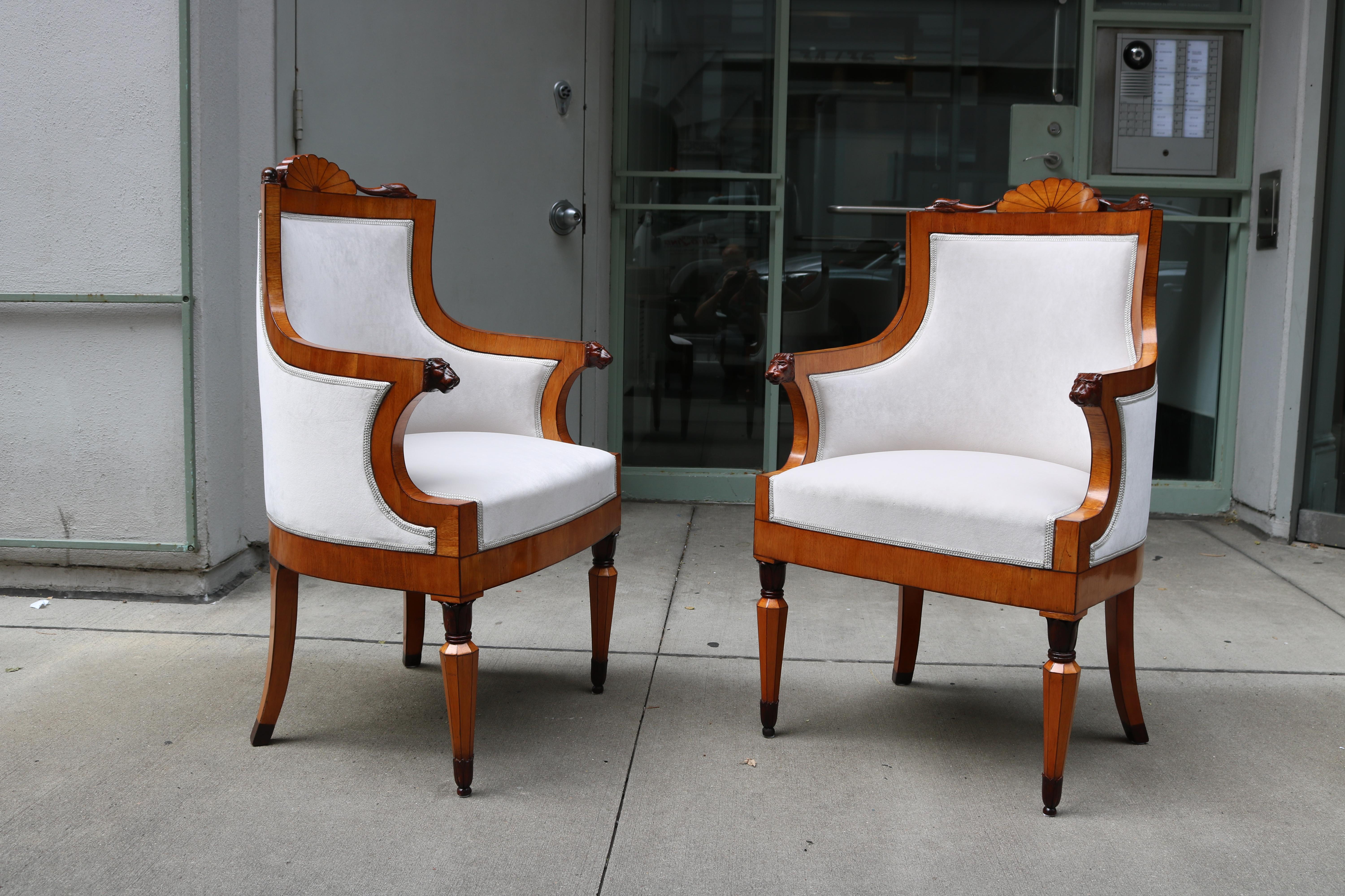 This exquisite pair of armchairs features high, rounded backrests and C-shaped armrests. They stand on octagonal legs with leaf capitals and bases as well as sabre legs. The intricate carved ornamentation includes lion heads on the armrests and