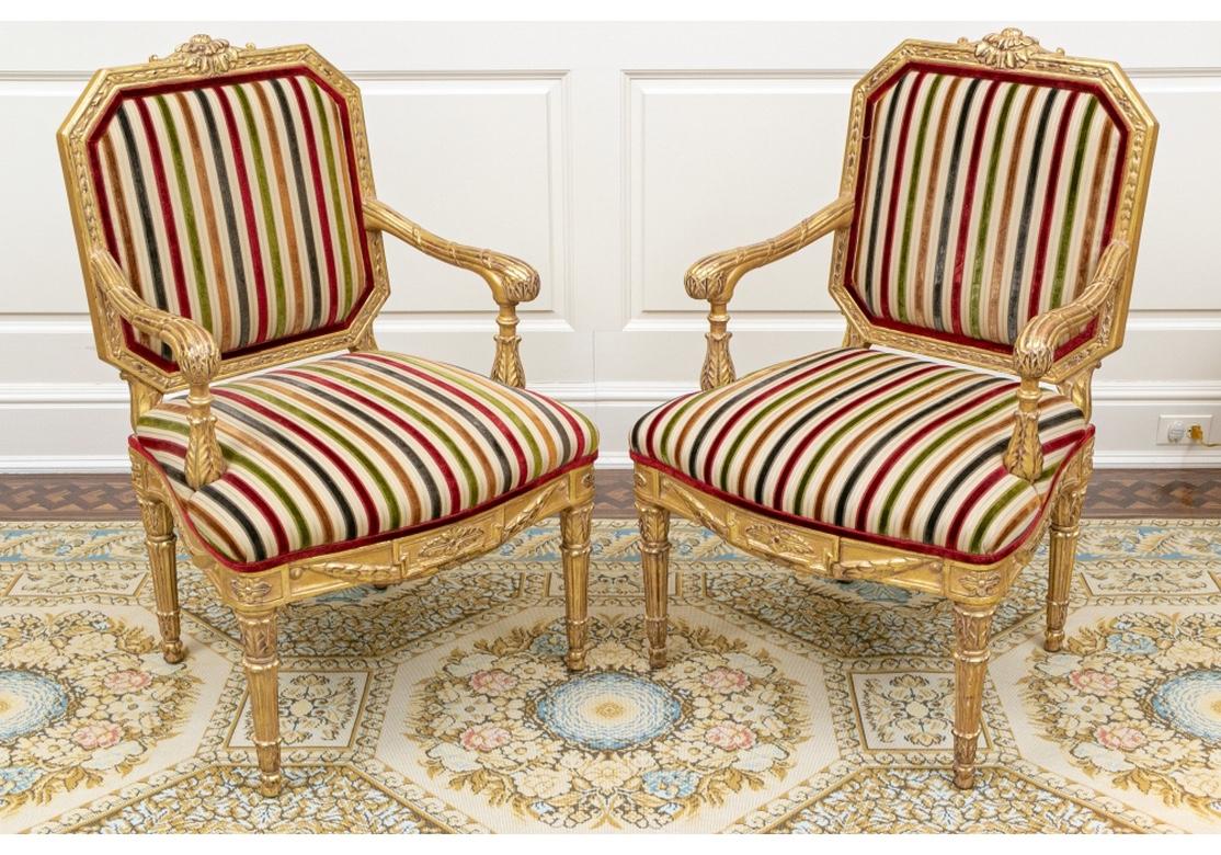 Large scale comfortable chairs with overall carved and gilt frames. The crest rails with scrolled flower centers and canted ends. Ribbed ribbon twist arms with leafy ends, the seat rails with swags on the sides, raised on fluted leafy legs.