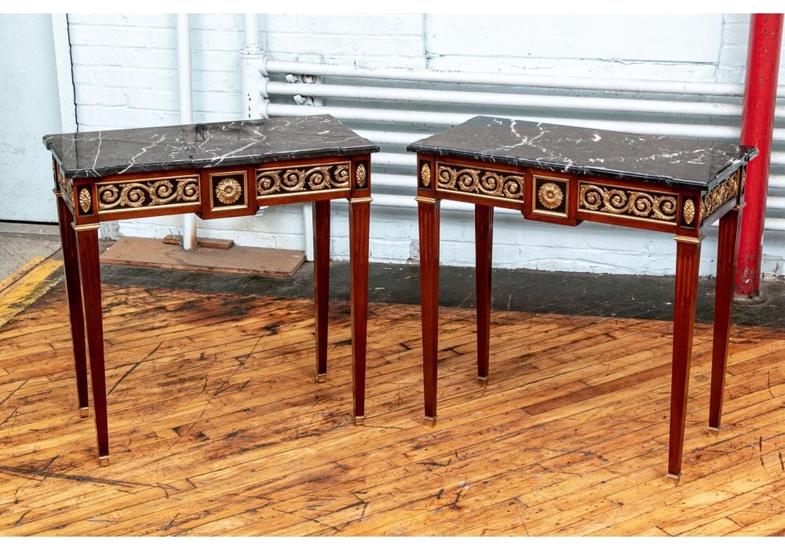 A very fine pair of console/pier tables in neoclassical style having good color and proportions. With mahogany frames and shaped black marble tops. The apron with ebonized panels with foliate scrolled brass appliques on front and the sides, and