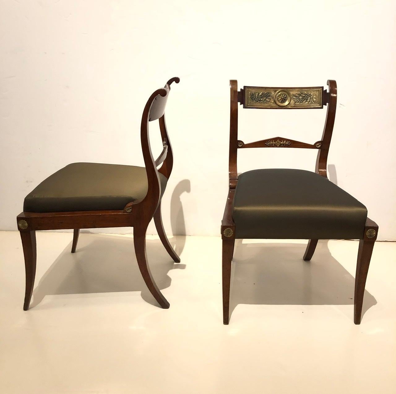 An elegant pair of Italian Neoclassical mahogany chairs adorned with patinated brass mounts from Italy. These chairs feature bold saber shaped legs and vertical lyre shaped back supports framing the unusual horizontal cross sections. Each chair back